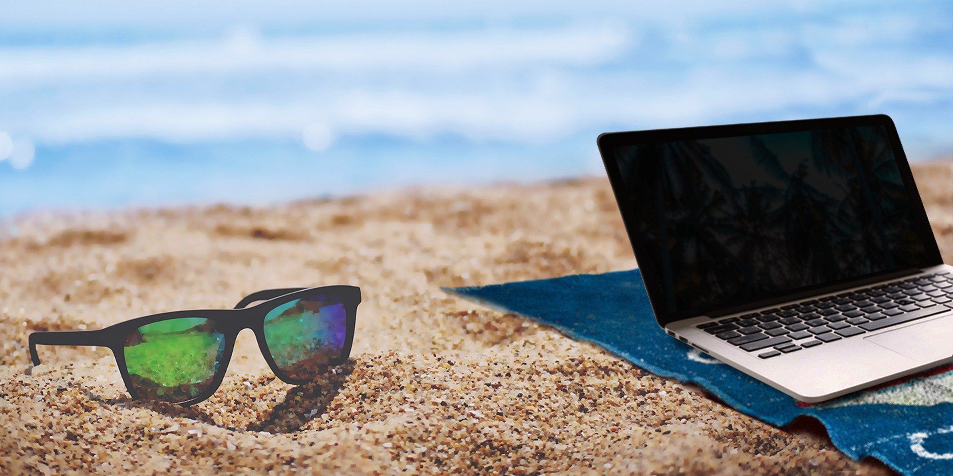 portátil encima de una toalla en la playa y con gafas de sol cerca